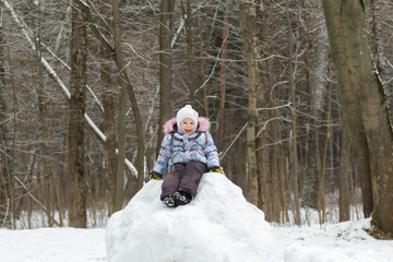 Fototapeta na wymiar Smiling little girl wearing warm clothes posing on snowy hill in winter forest