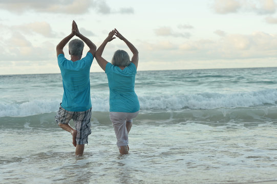 elderly couple doing yoga on beach