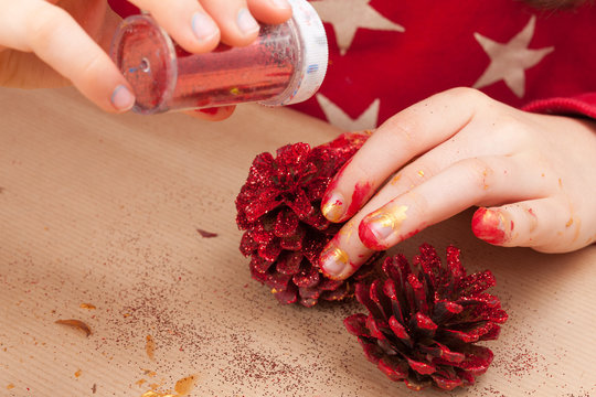 Child putting glitter on a painted pine cone.
