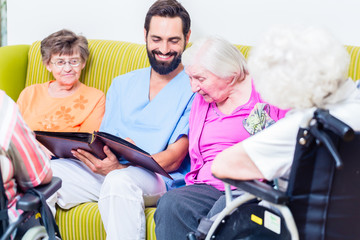 Altenpfleger schaut Fotos mit Senioren im Altenheim an