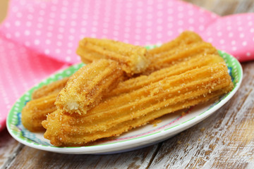 Freshly made Spanish churros on plate with pink cloth in the background
