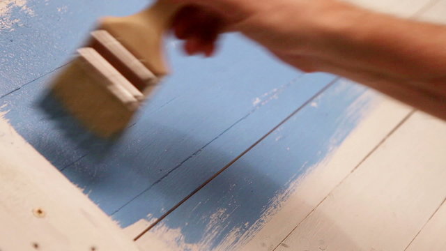 Wooden board's painting process: an artist applies blue colour with a brush