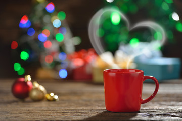 Cup of coffee with heart-shaped smoke surrounded by Christmas decorations on Christmas lights bokeh background