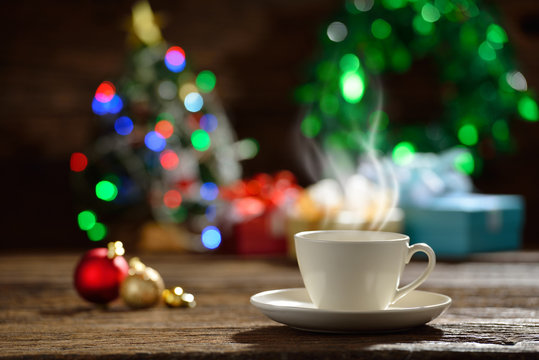 Cup of coffee with smoke surrounded by Christmas decorations on Christmas lights bokeh background