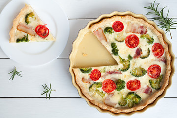 Sliced quiche lorraine traditional homemade french tart pie preparation recipe with tomatoes bacon cheese and broccoli on white vintage table background