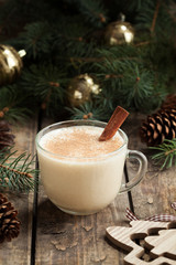 Traditional eggnog homemade christmas non alcohol winter drink in glass cup with cinnamon stick on vintage wooden table. Xmas fur decorations