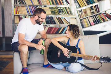 Young couple sitting on a couch with a guitar. The woman is playing the guitar.