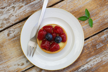 Crunchy and creamy tartelette with raspberries and blueberries on rustic wooden surface
