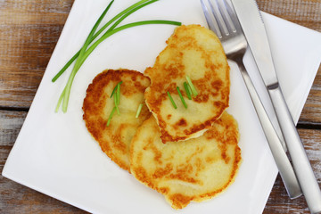 Potato fritters garnished with spring onions on white plate on rustic wooden surface

