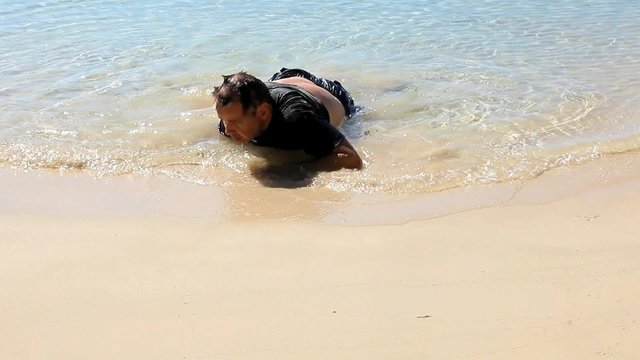 exhausted man crawled out of the sea and lying on the beach