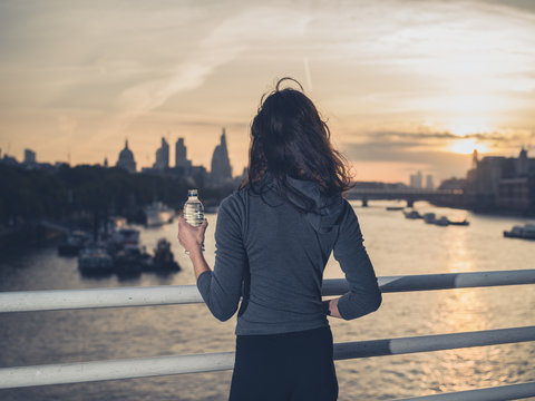 Sporty young woman with bottle on bridge at sunrise