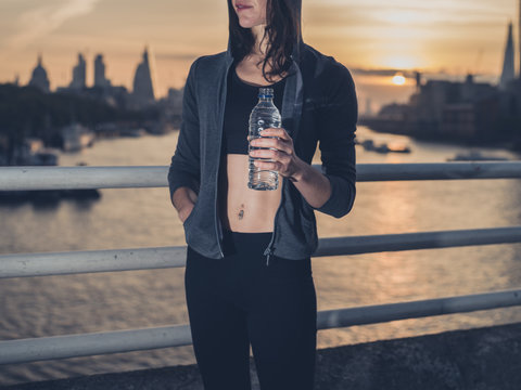 Fit young woman with bottle in city at sunrise