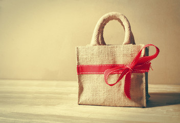 Beautiful gift bag with red bow on wood background and color filters