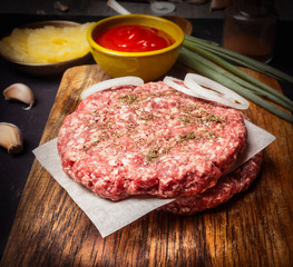 Raw Ground beef meat Burger steak cutlets  with onion rings, sauce on a cutting board on wooden rustic background  close up