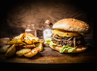 delicious homemade burger with meat, onions, lettuce and pineapple, potato wedges on wooden rustic...