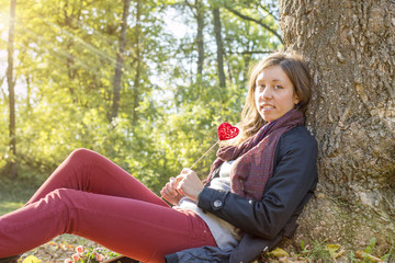 Beautiful girl holding red heart on a stick while sitting on the