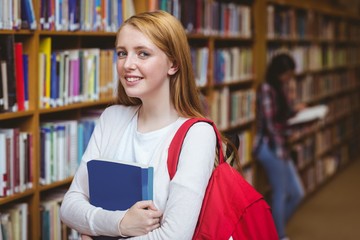 Smiling student with backpack holding a book in library