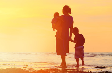mother and two kids walking on beach at sunset