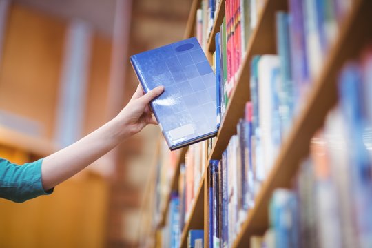 Students hand with smartwatch picking book from bookshelf