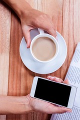 Part of hands holding coffee and smartphone