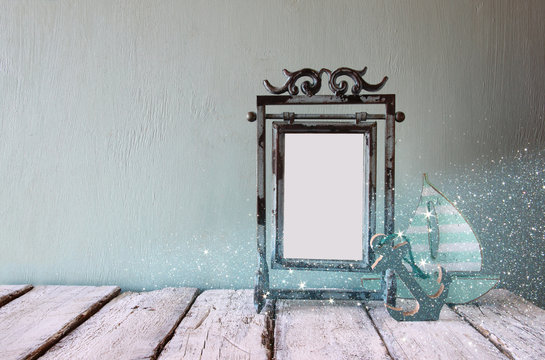 low key image of old victorian steel blue blank frame and wooden sailing boat on wooden table