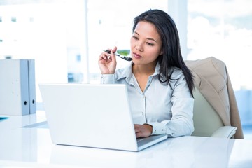 Smiling businesswoman with pen using laptop 