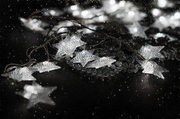 Illuminating stars and crystal beads on the black background with white bokeh and snowfall.