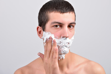 Closeup of a young man preparing to shave, he puts foam on his c