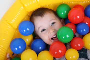 Fototapeta na wymiar Little smiling boy playing in colorful balls playground
