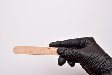 A beauticians hand with black glove holding a spatula for wax, p