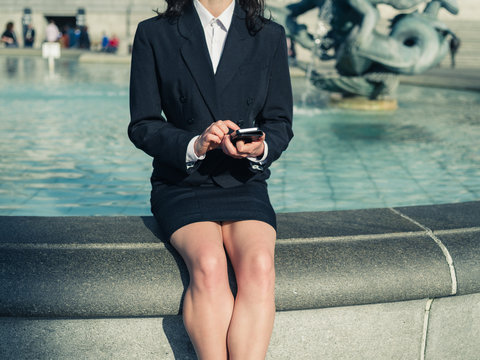 Young businesswoman using smart phone by fountain