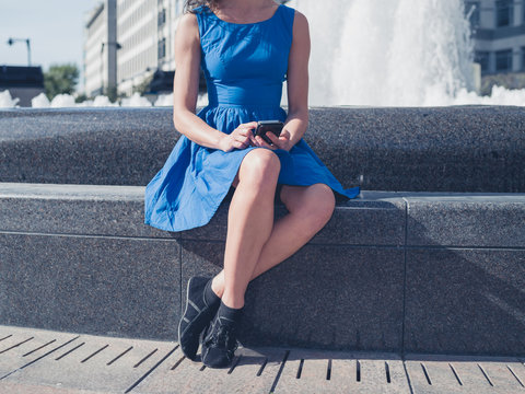 Young woman using smart phone by fountain in city