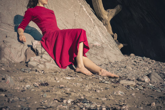 Woman in red dress relaxing by cave on beach