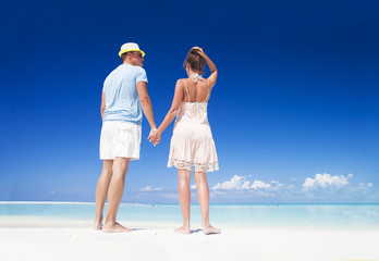 back view of romantic couple in bright clothes enjoying sunny day at tropical beach