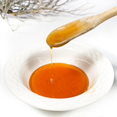 Pouring thyme honey into a ceramics bowl with a wooden spoon. Thyme branch at background