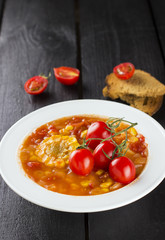Corn soup with cherry tomatoes in white plate against a dark bac