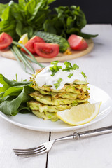 Zucchini fritters on white plate with sour cream, sorrel and lem