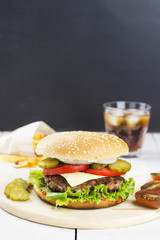Burger with vegetables, french fries and drink on a wooden backg