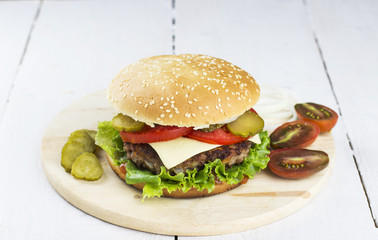 Big burger with lettuce, cutlet, tomato, cheese on a white woode