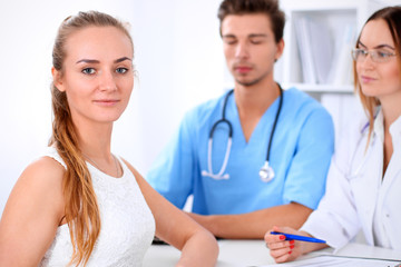Fototapeta premium Happy blond female patient next to a few doctors in hospital sitting at the table