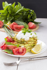 Zucchini fritters on white plate with sour cream, basil, tomatoe