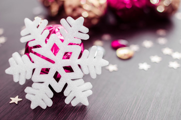 White snowflake on background of magenta and gold xmas baubles with space for text. Merry christmas. Winter holidays. Xmas theme. Happy New Year. Blurred background.