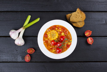 Corn soup with cherry tomatoes in white plate on wooden backgrou
