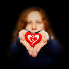 Young girl holds in her hands red heart surrounded by darkness