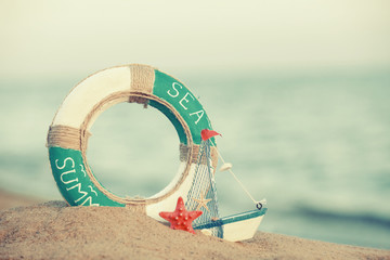 Beautiful life buoy in the sand with boat toy on unfocused sea background