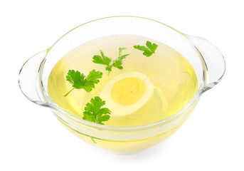 Low-fat chicken broth with a half cooked egg and parsley in a glass bowl isolated on white background.