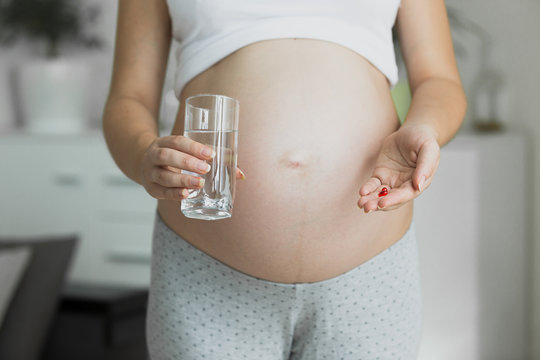 Toned photo of pregnant woman with glass of water and pills