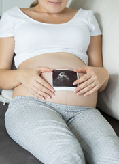 Closeup of pregnant woman holding ultrasound image on stomach