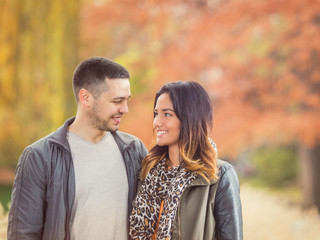 Portrait of a happy young couple looking at each other while walking through the park in autumn