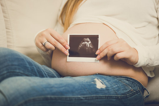 toned photo of pregnant woman posing with ultrasound abode image